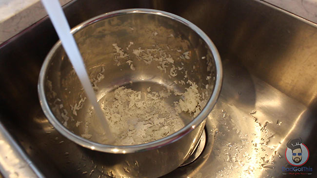 Water pouring into the stainless steel inner pot with leftover rice in it.