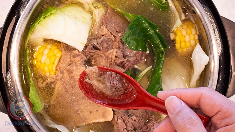 A soup spoon over and Instant Pot with Beef Bulalo Soup in it.