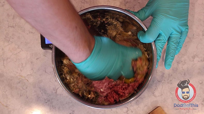 a gloved hand mixing ground beef and pork in a silver bowl for meatballs