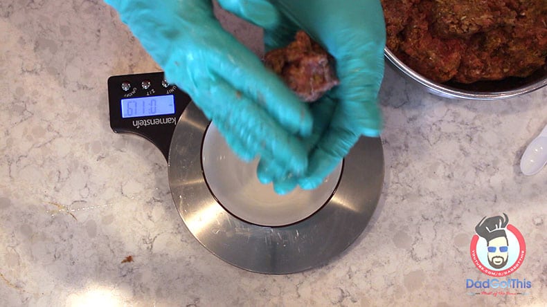 gloved hands rolling meatball mixture into a ball