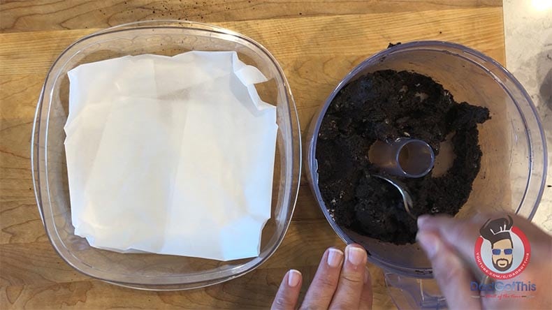 A container lined with wax paper next to a food processor bowl with oreo truffle dough in it