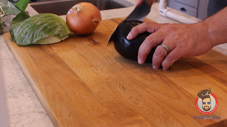 an eggplant being chopped with onion and cabbage in background