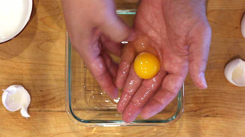an egg yolk in the palm of a hand over a glass bowl