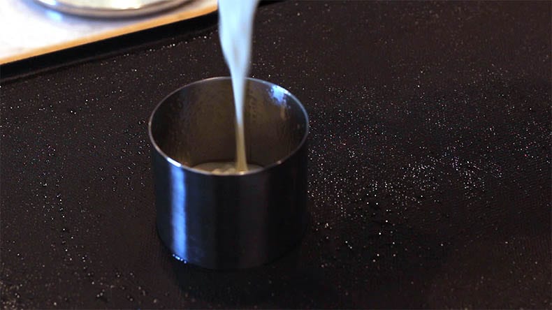 a stainless steel ring on an electric griddle with batter being poured in it