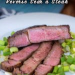 A reverse seared steak on a white plate with scallions