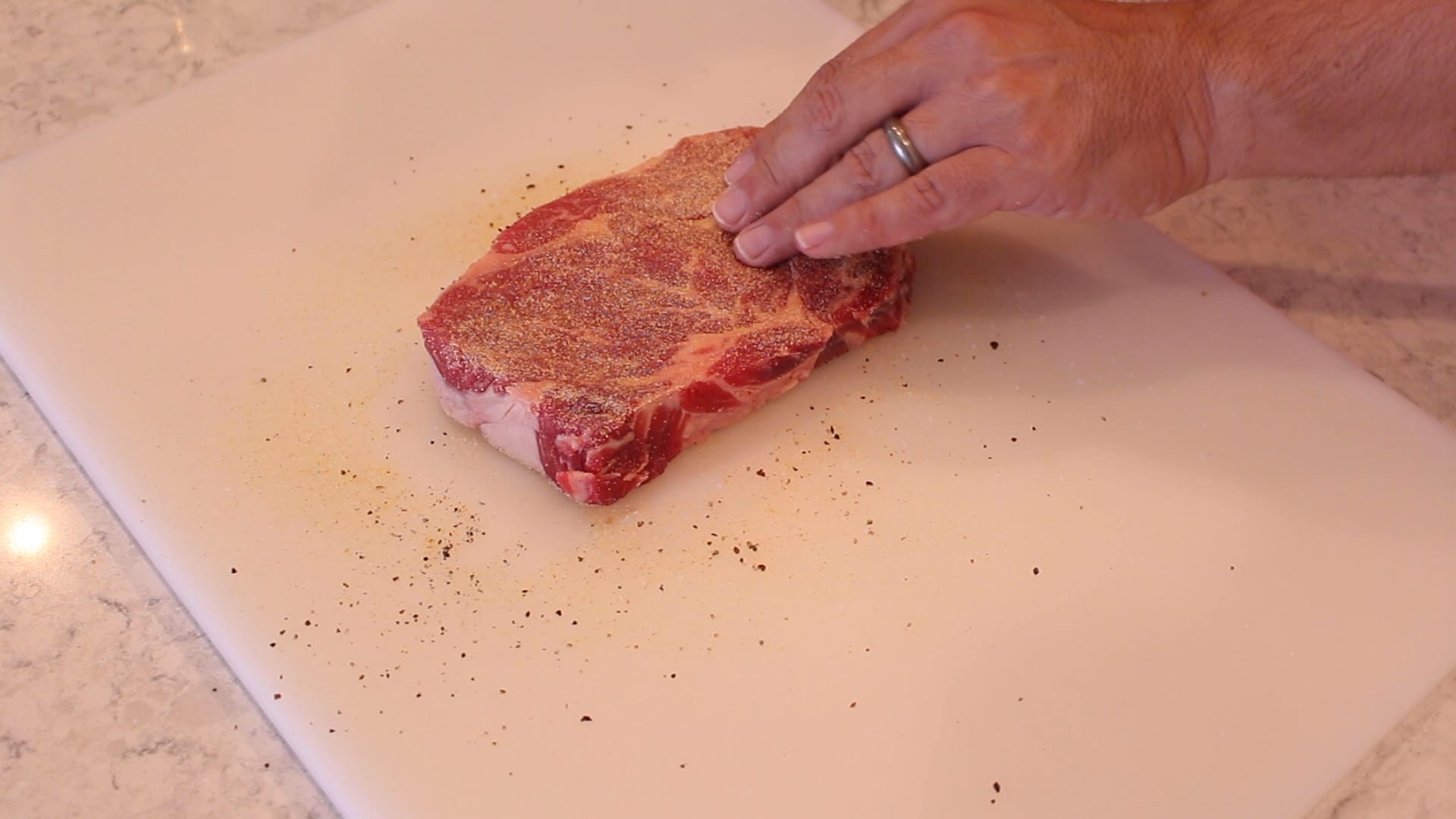 A ribeye steak being seasoned