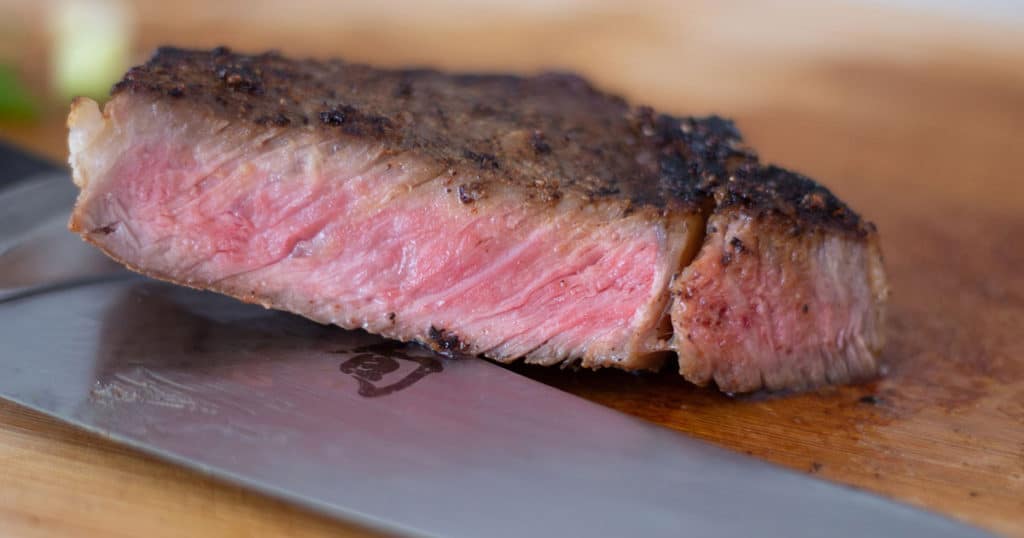 A reverse seared steak cut on a cutting board with a knife