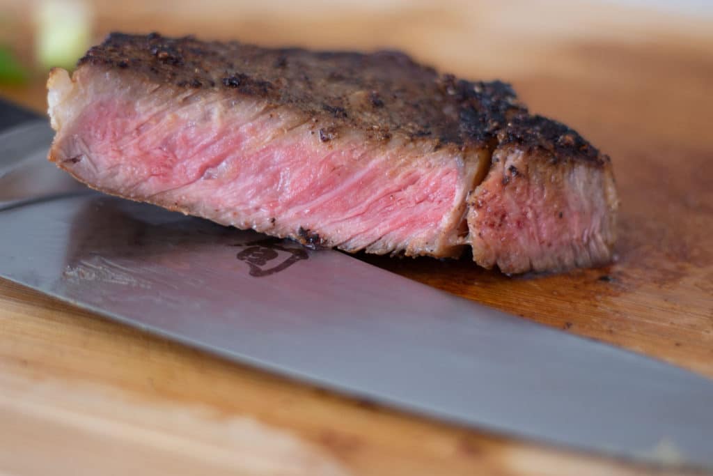 A reverse seared steak cut on a cutting board with a knife