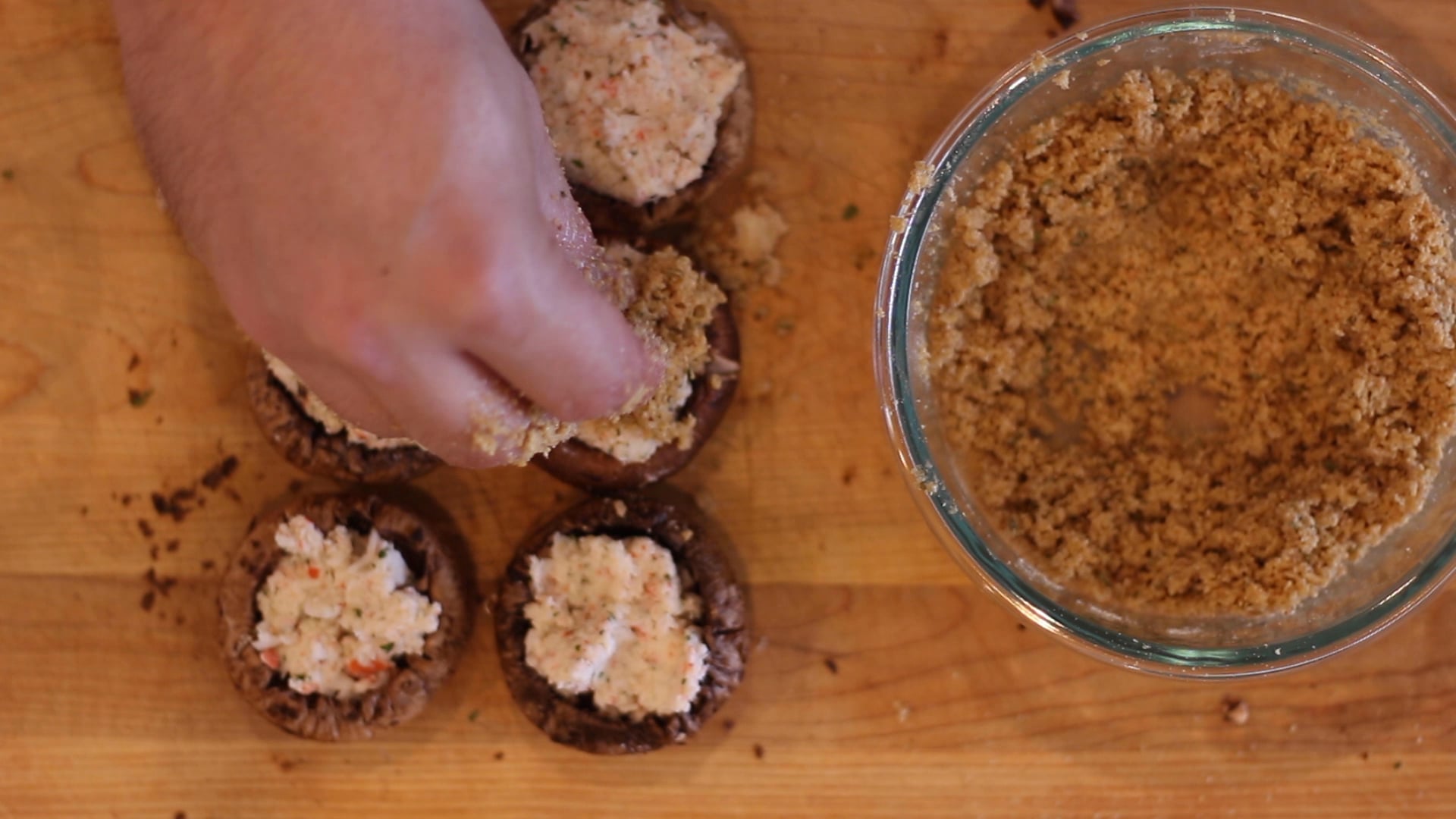 A hand placing a topping on crab stuffed mushrooms