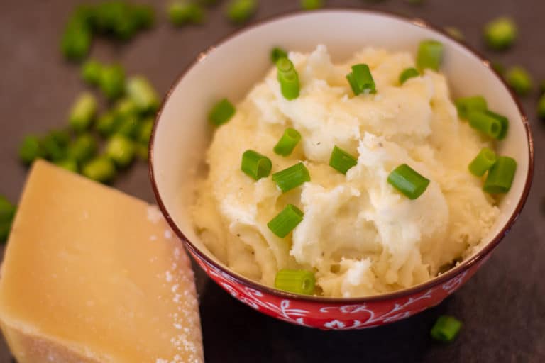 parmesan mashed potatoes in a bowl next to parmesan cheese