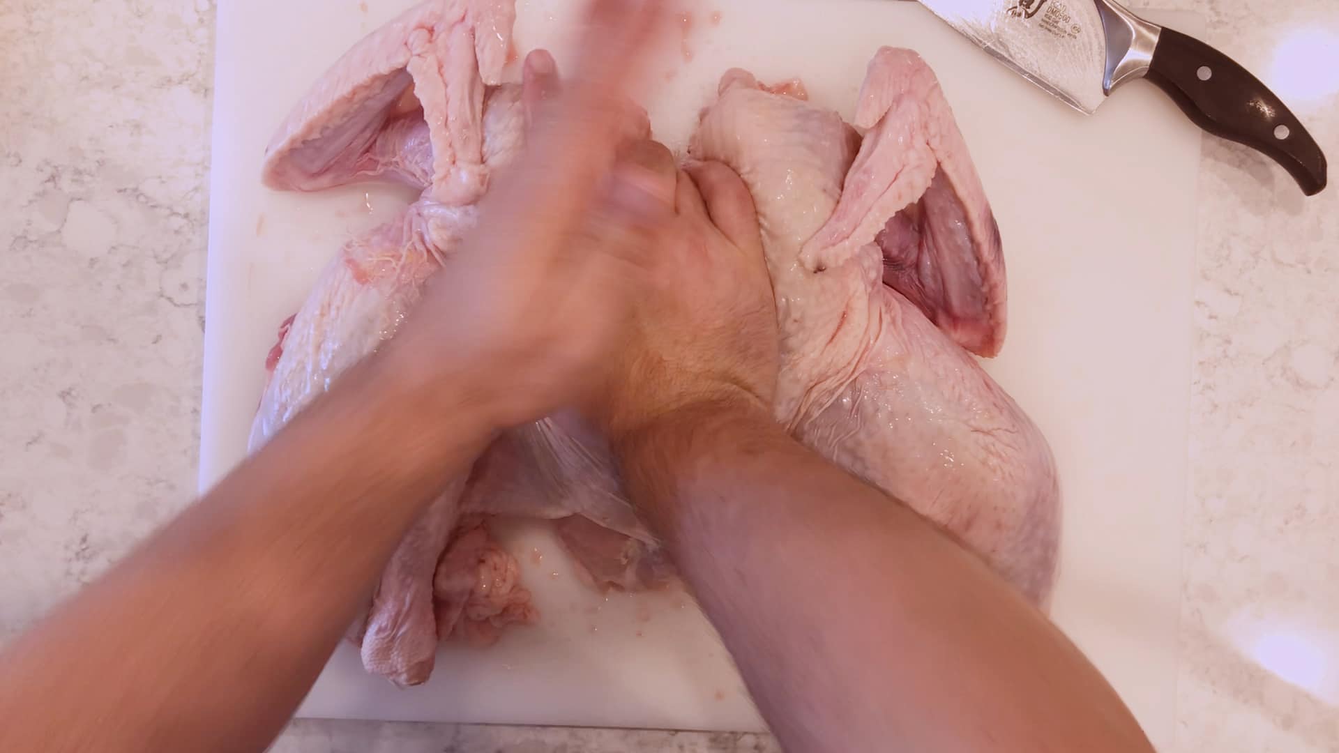 Hands pressing down on a spatchcocked turkey