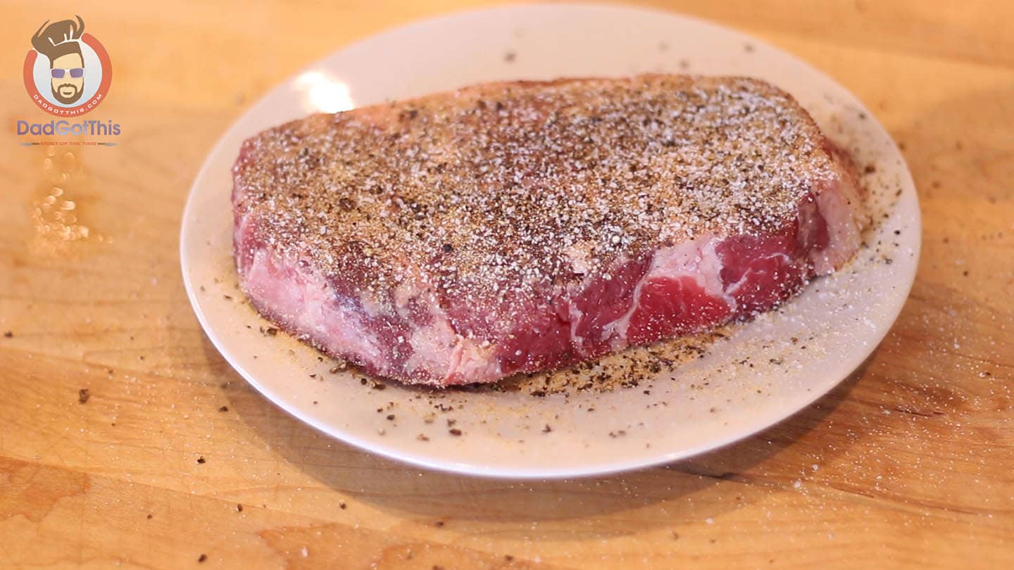 a raw ribeye steak on a plate being seasoned