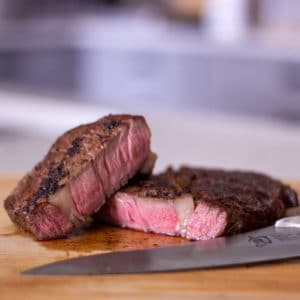 A cut ribeye steak with a knife on a cutting board