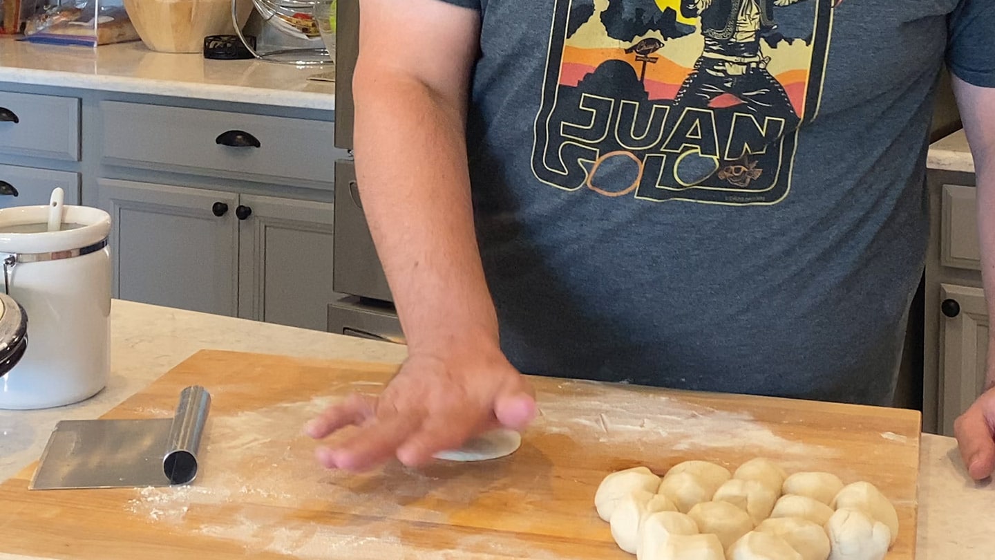 pressing dough balls flat on a cutting board