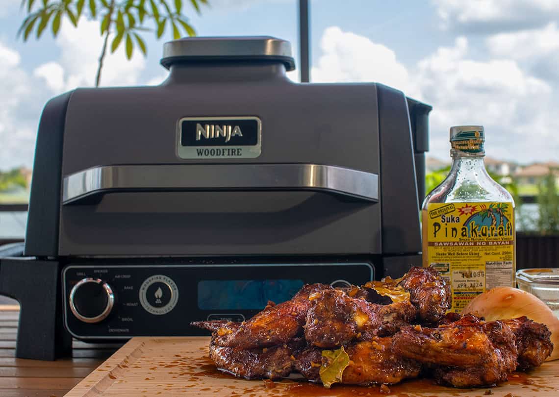 Adobo Style Chicken Wings in front of a Ninja Woodfire Grill.