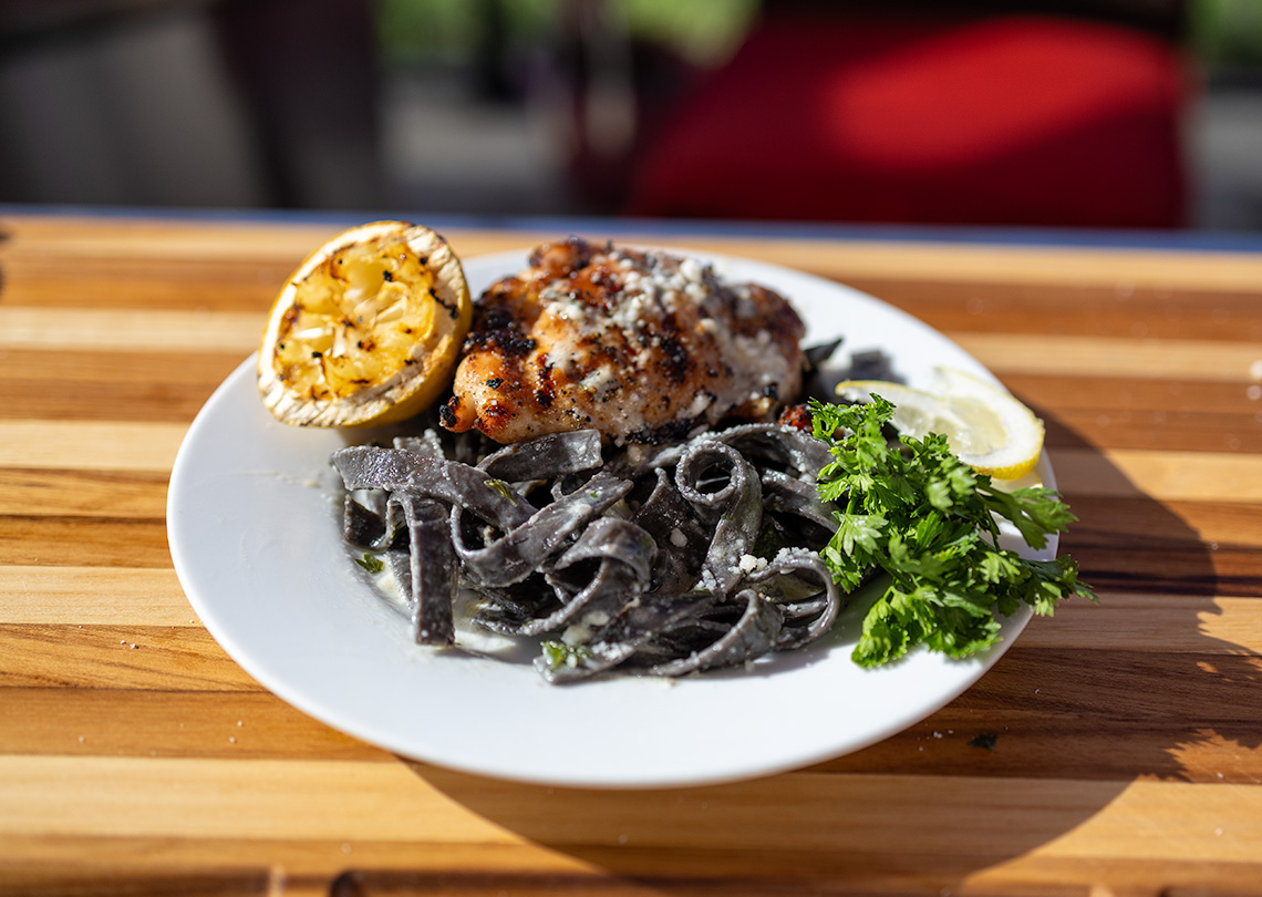 Grilled Chicken with squid ink pasta on a plate.