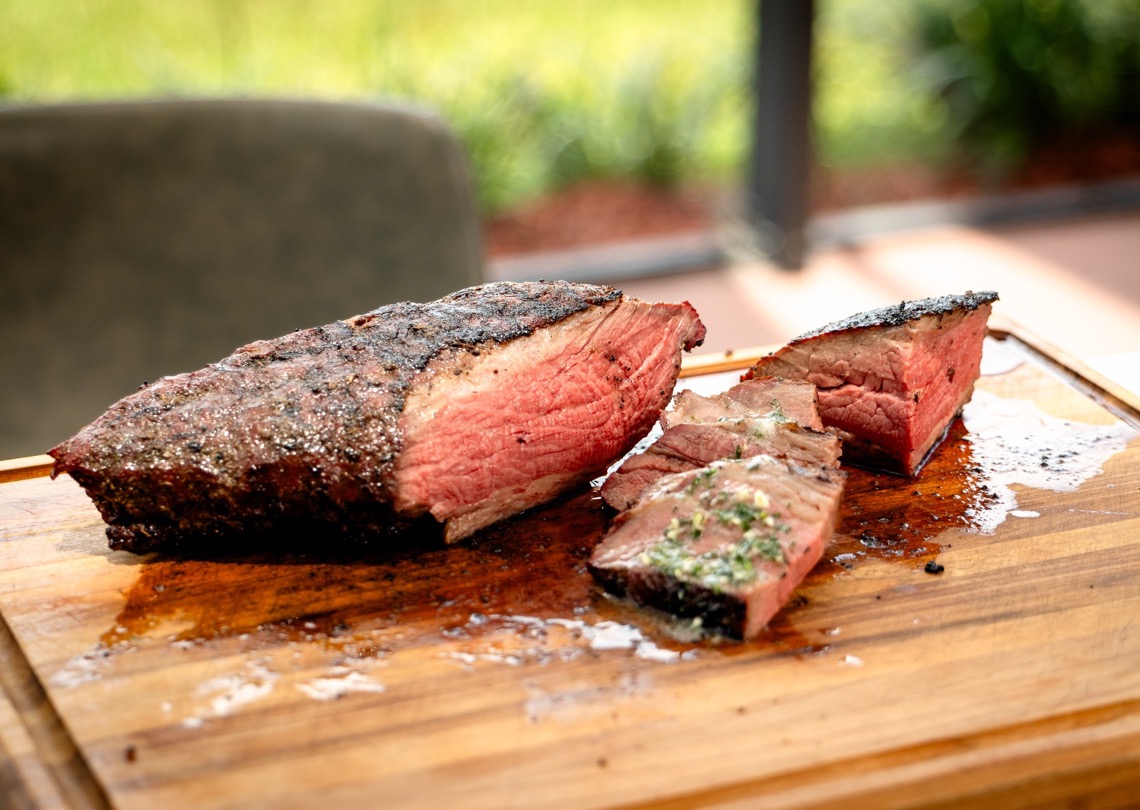 Sliced tri tip cooked like prime rib with fresh herb butter on a cutting board.
