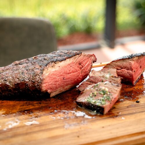 Sliced tri tip cooked like prime rib with fresh herb butter on a cutting board.