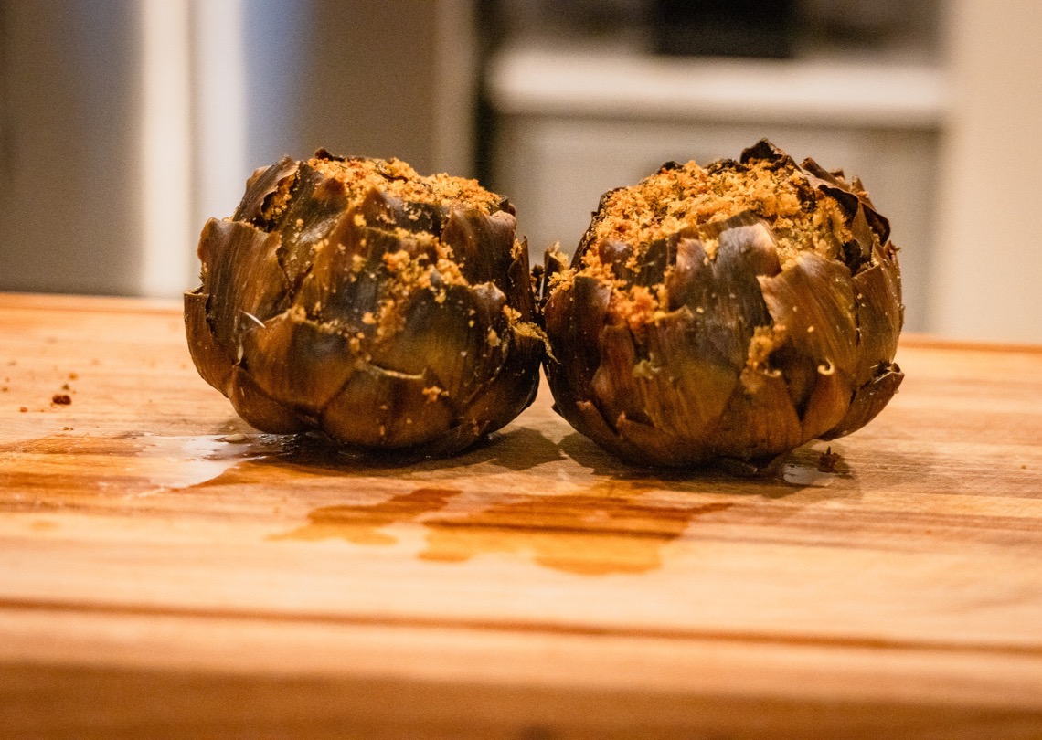 Two Woodfire smoked Italian stuffed artichokes on a wooden cutting board