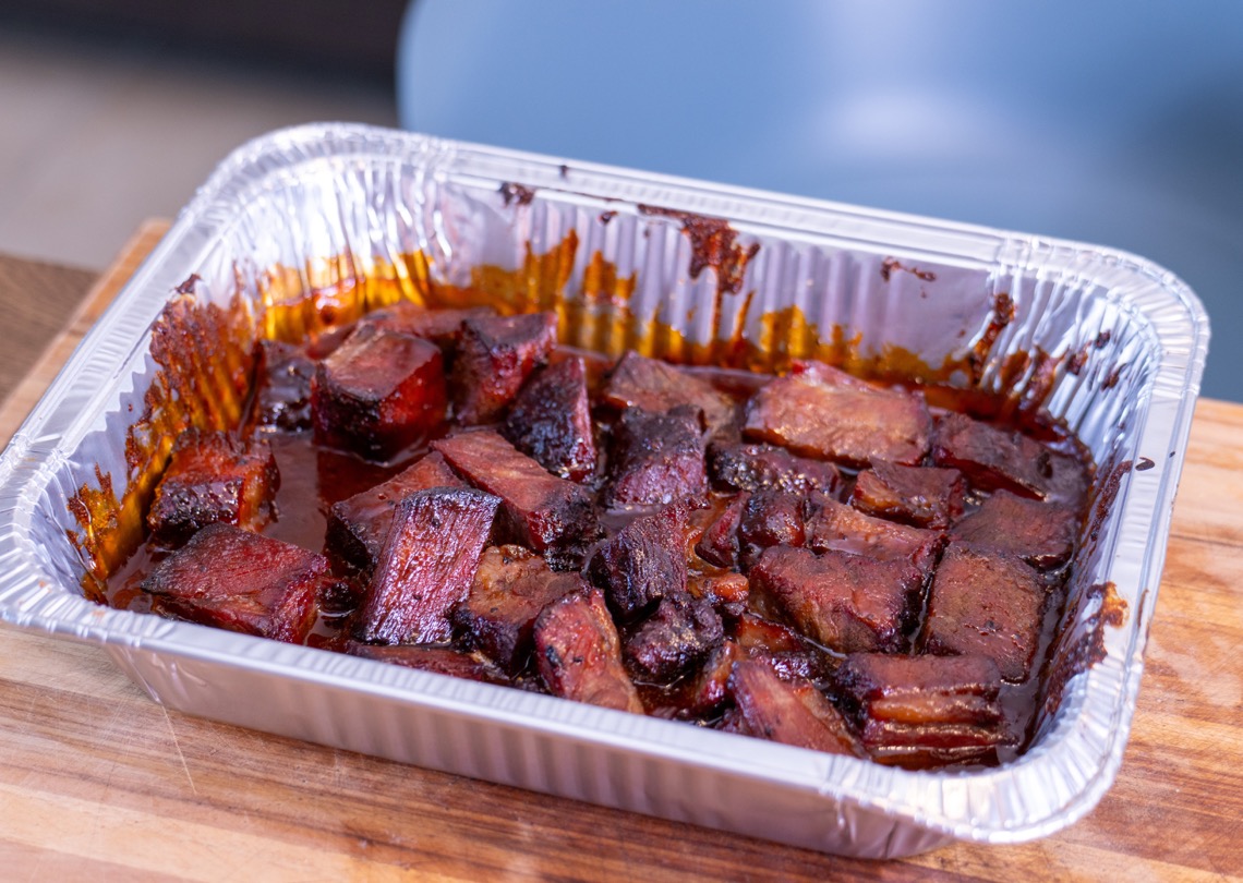 Chuck Roast Burnt Ends coated in barbecue sauce in an aluminum pan