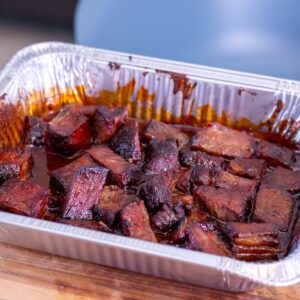 Chuck Roast Burnt Ends coated in barbecue sauce in an aluminum pan