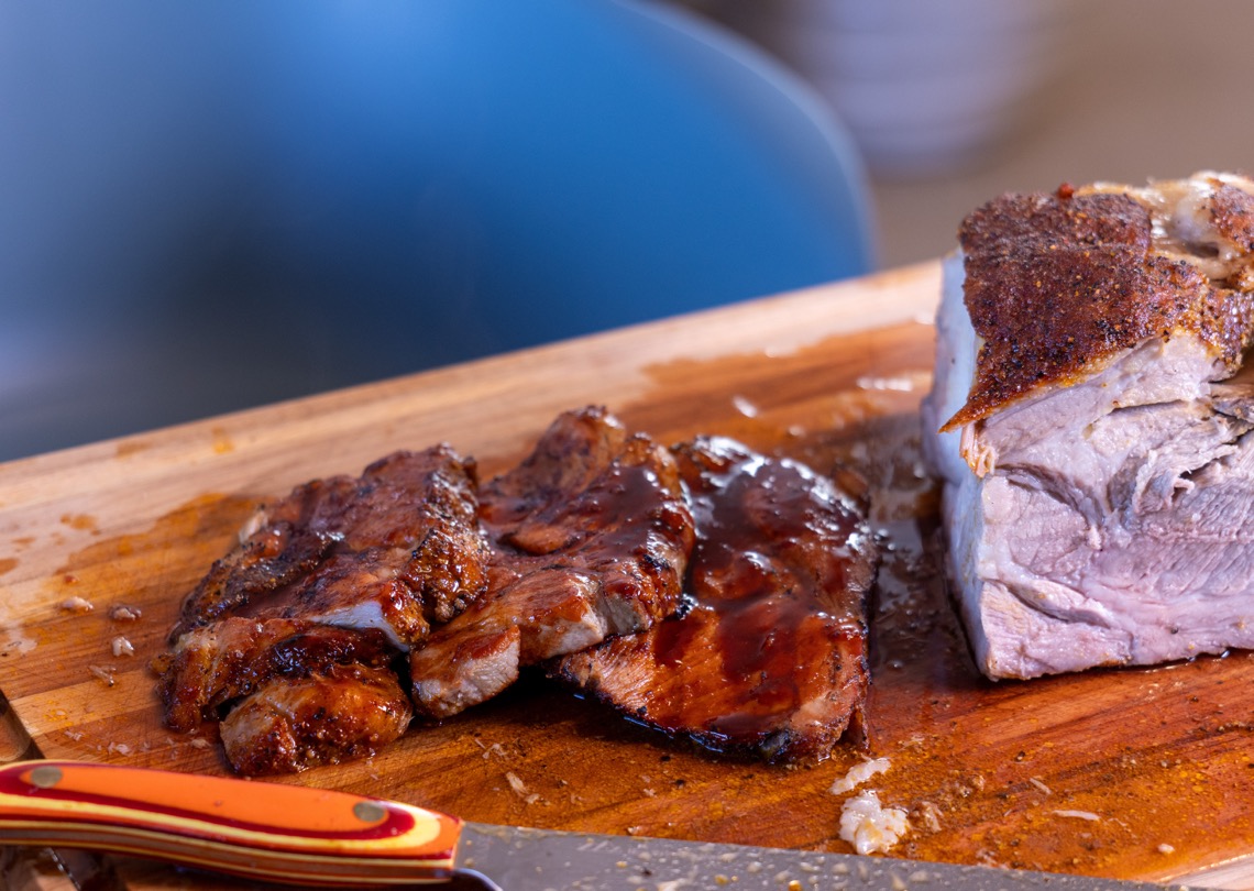Sliced Filipino BBQ style pork glazed with banana ketchup sauce beside a smoked pork roast