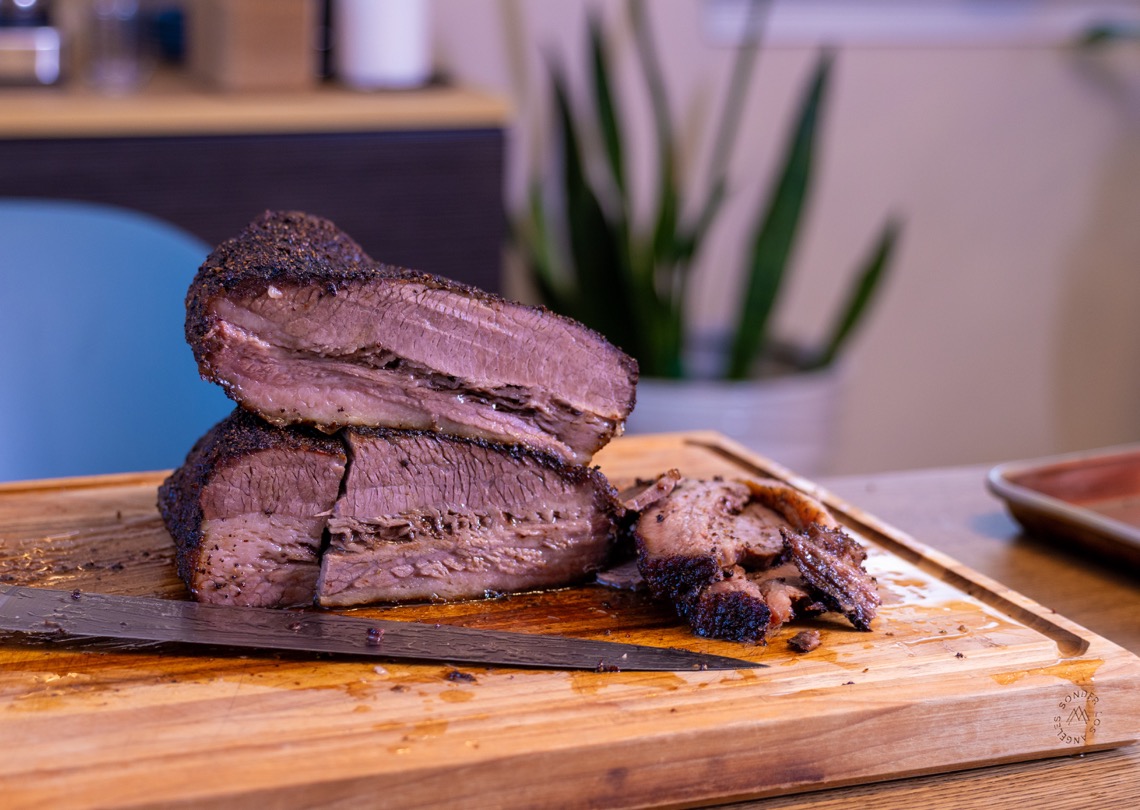 Sliced Ninja Woodfire brisket with dark bark on a wooden cutting board