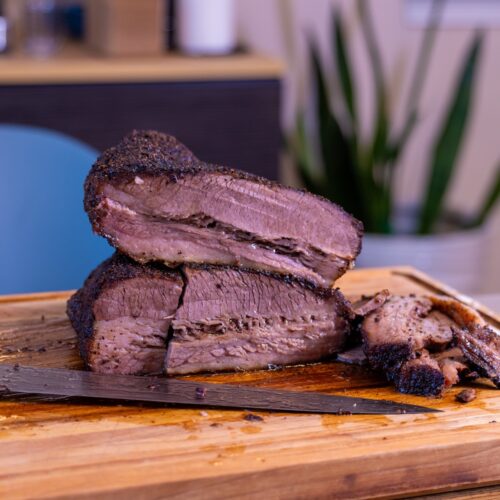Sliced Ninja Woodfire brisket with dark bark on a wooden cutting board