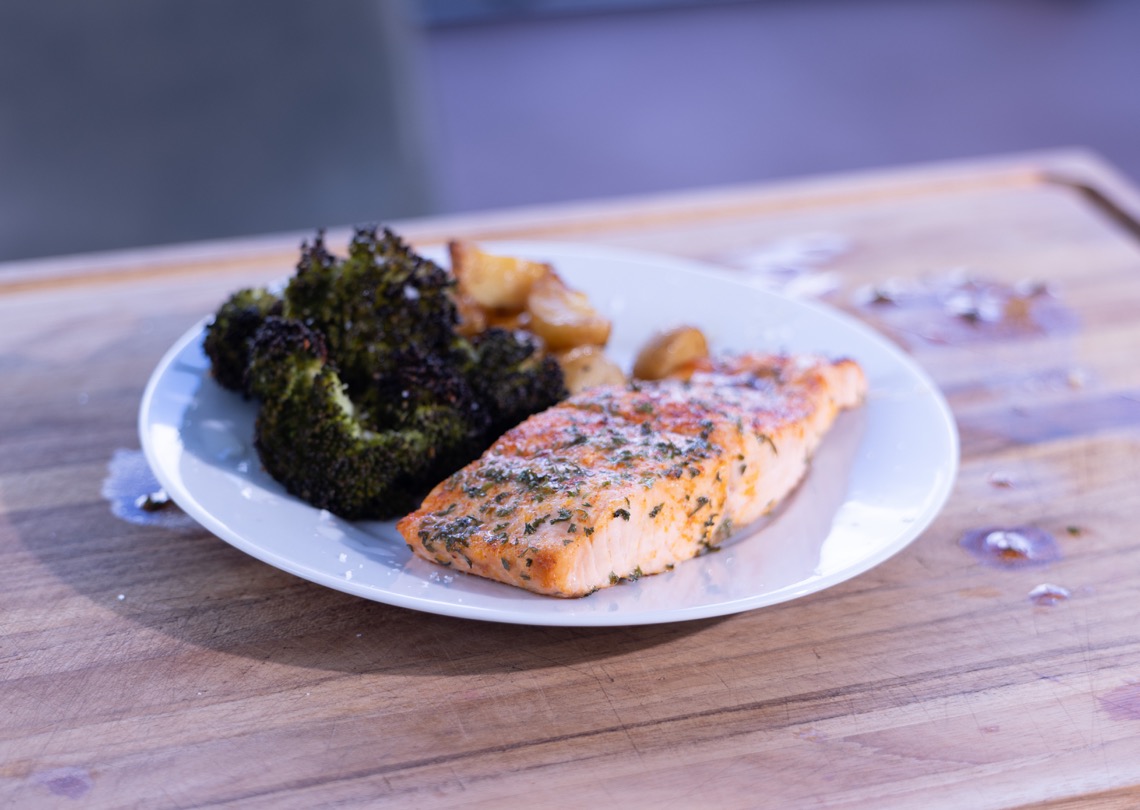 Ninja Woodfire salmon dinner with roasted potatoes and broccoli on a white plate
