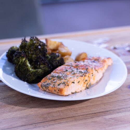 Ninja Woodfire salmon dinner with roasted potatoes and broccoli on a white plate