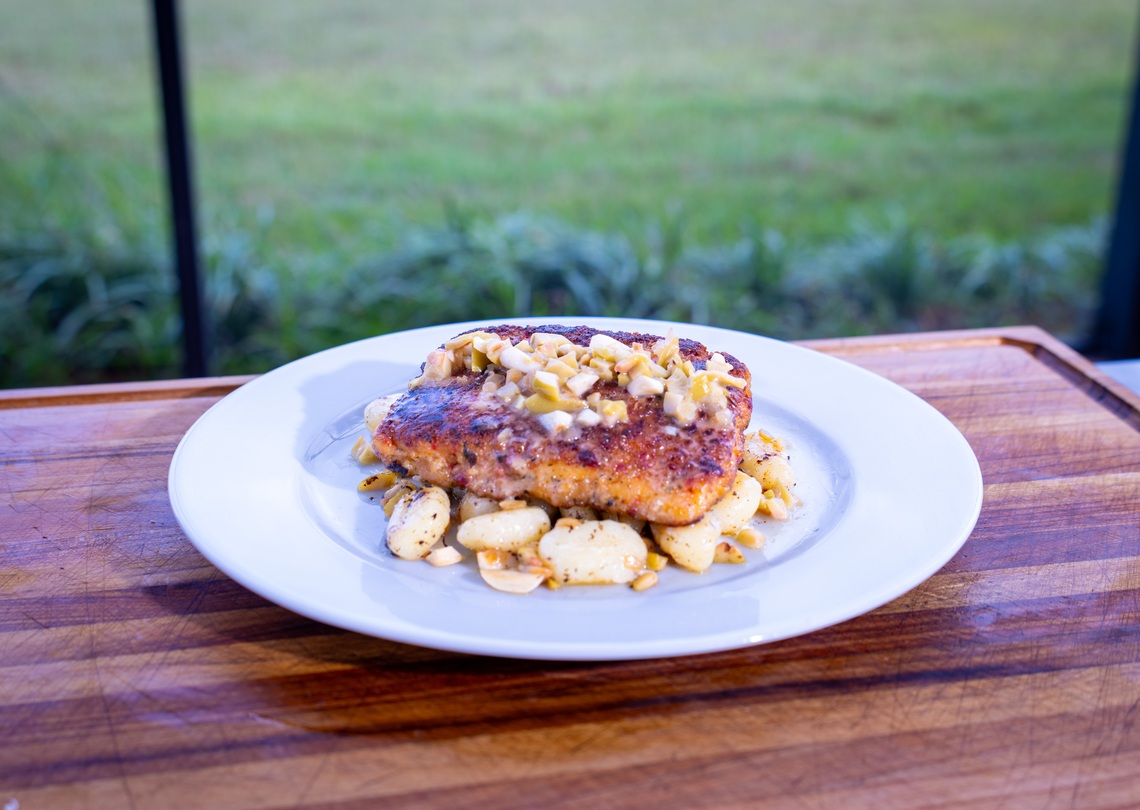 Mediterranean salmon topped with chopped garlic stuffed olives over gnocchi on a white plate.