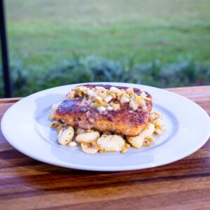 Mediterranean salmon topped with chopped garlic stuffed olives over gnocchi on a white plate.