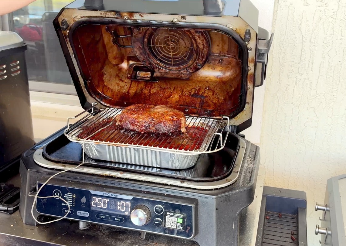 Ground chuck smoking on a rack above a foil pan of chili in the Ninja Woodfire