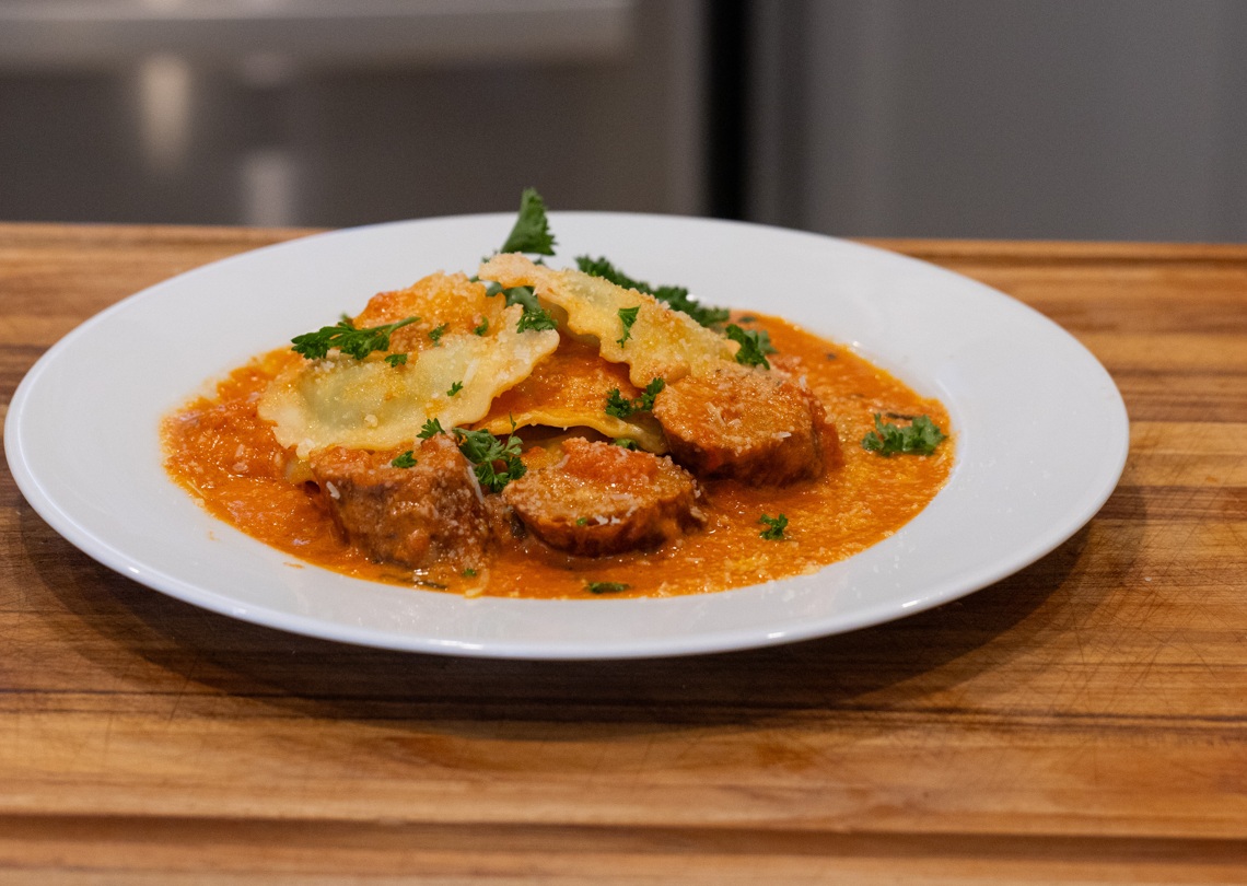 Smoked Italian sausage and ravioli in tomato basil cream sauce on a white plate
