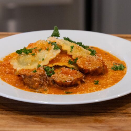 Sliced smoked Italian sausage and ravioli in tomato basil cream sauce on a white plate
